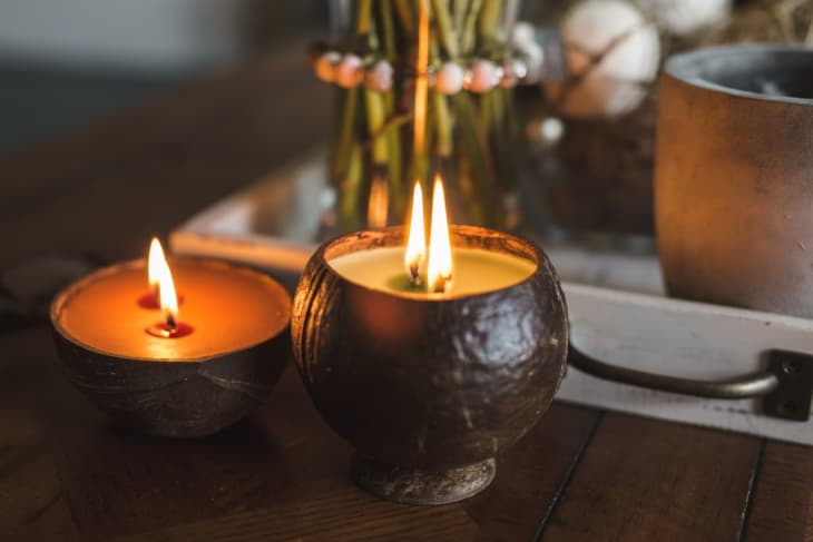 Two lit coconut shell candles on a wooden table with a decorative tray in the background.