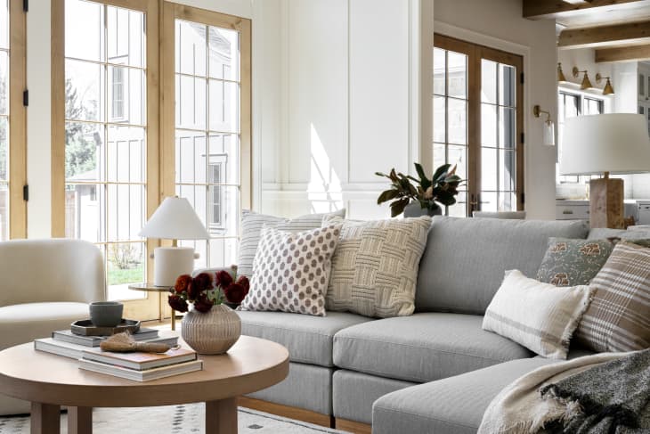 Cozy living room with a gray sectional sofa, patterned pillows, round coffee table, and large windows.