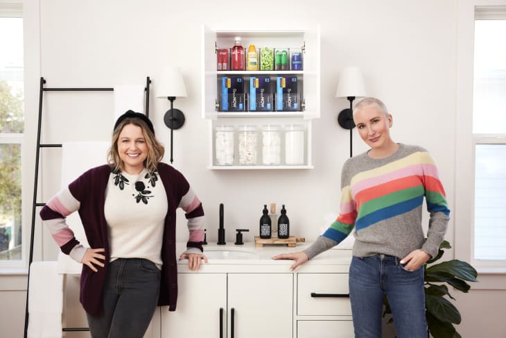 Joanna Teplin and Clea Shearer of The Home Edit with an organized, colorized medicine cabinet in a bathroom with white cabinetry