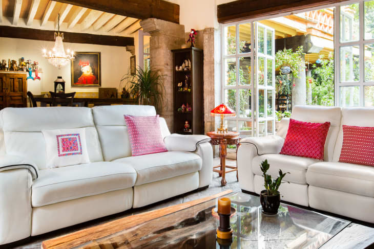 Airbnb living room in Mexico City with large windowed french doors open to lush patio, white sofas, red patterned throw pillows, dining room in background