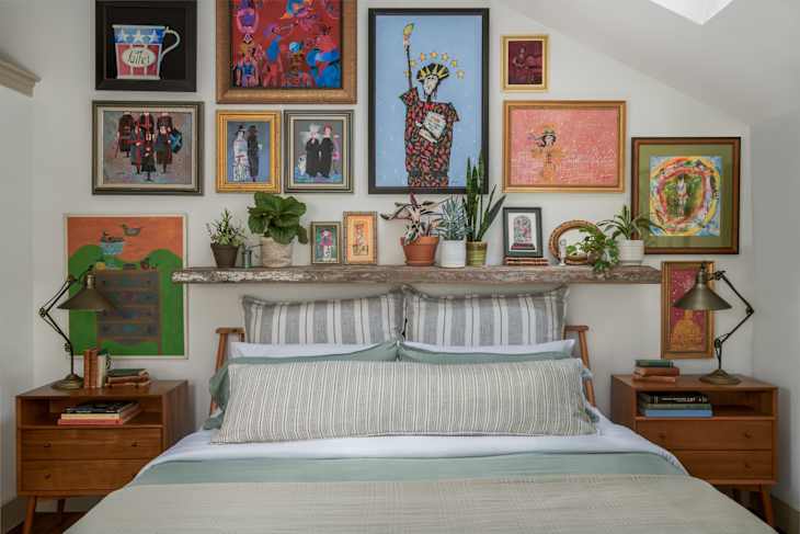 Colorful gallery wall above a bed with striped pillows, wooden nightstands, and various plants.