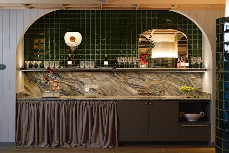 A stylish bar area featuring a green tiled wall, marble countertop, and glassware.