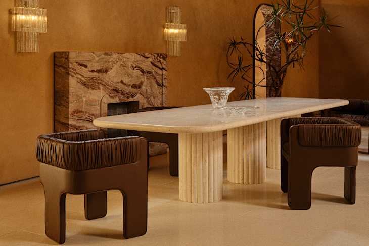 A modern dining area featuring a long stone table, two brown upholstered chairs, and a decorative glass bowl.