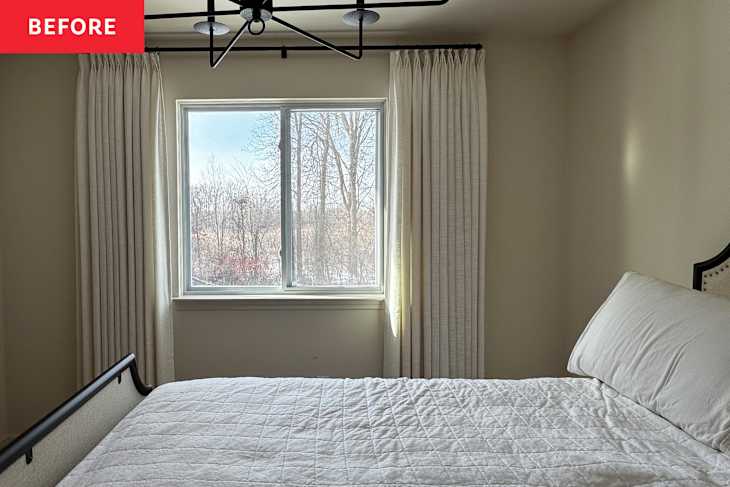 A bright bedroom with a window dressed in light curtains, a white quilted bedspread, and a black metal bed frame.