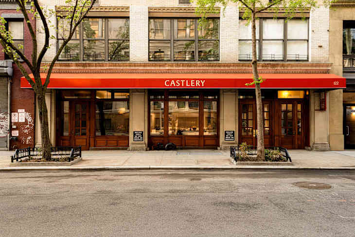 Facade of a restaurant named Castlery with a red awning, large windows, and wooden doors, surrounded by trees and benches.