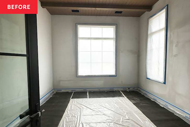 Empty room with unpainted walls, large window covered in plastic, and protective sheets on the floor.