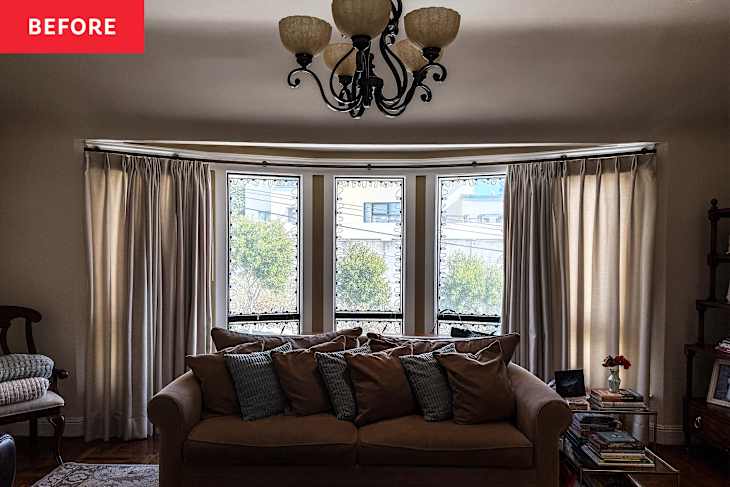 Cozy living room with a brown sofa, decorative pillows, large windows with curtains, and a chandelier.