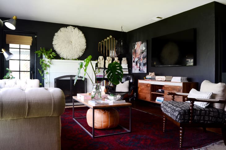 Living room with dark walls, white fireplace, large wall art, tufted sofa, wooden furniture, and green plants.