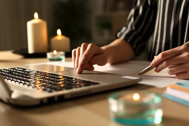 夜间，在停电的情况下，女企业家的手在家里办公室的桌子上拿着蜡烛工作