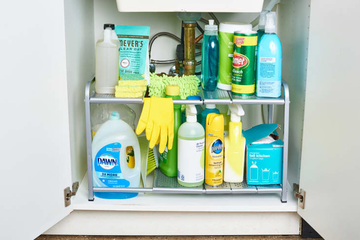 Cleaning supplies on a tiered shelf in a cabinet