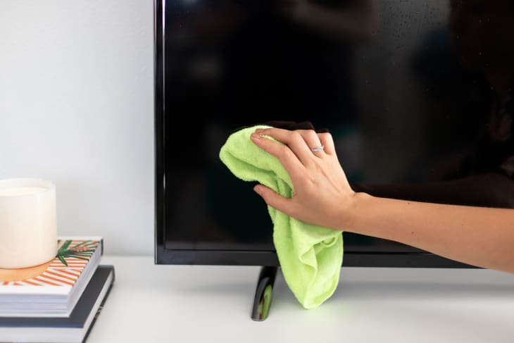 A person drying off their freshly-cleaned television screen with a dry microfiber cloth