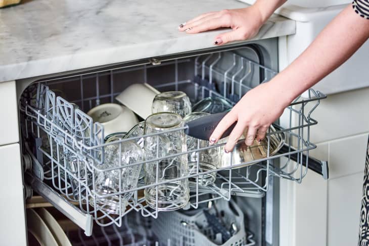 A person is pushing the top rack in of a dishwashing machine