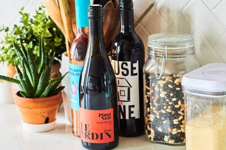 Wine bottles, potted plants, and jars of grains on a kitchen counter.