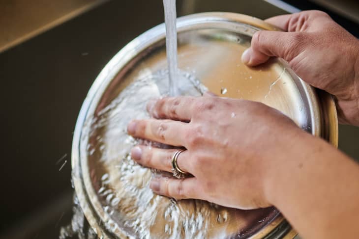 Rubbing hand on stainless steel pot lid with water running