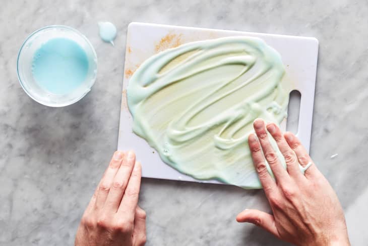 Hand smearing baking soda, hydrogen peroxide and Dawn liquid soap cleaning solution onto plastic cutting board.