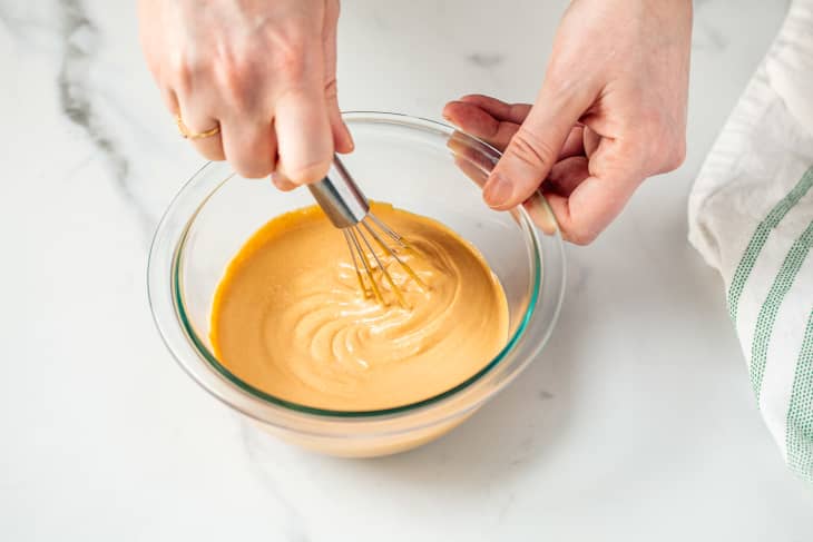 Someone whisking sauce in glass bowl.