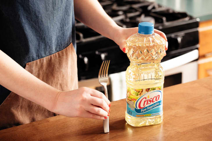 Someone holding fork upright next to bottle of vegetable oil.