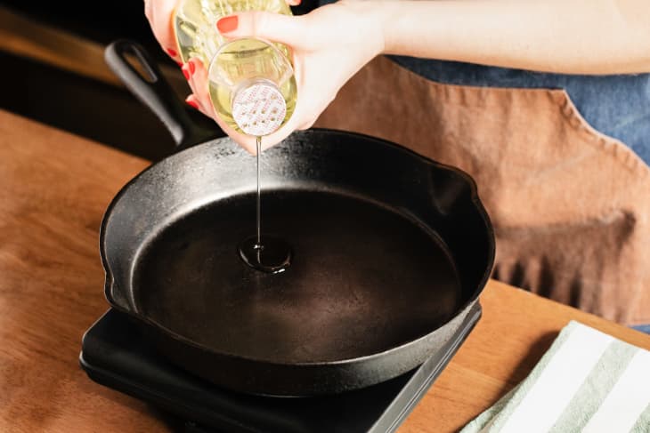 Someone pouring vegetable oil into cast iron skillet.