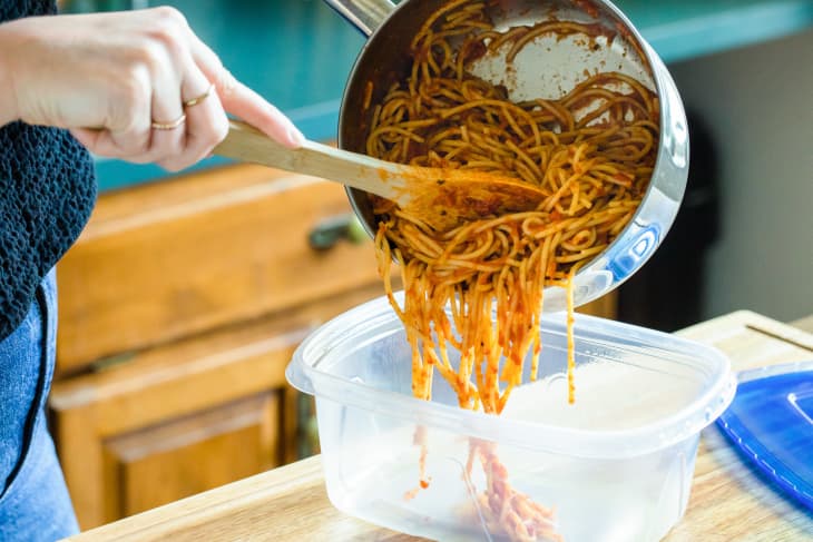 Someone scooping spaghetti leftovers into food storage container.