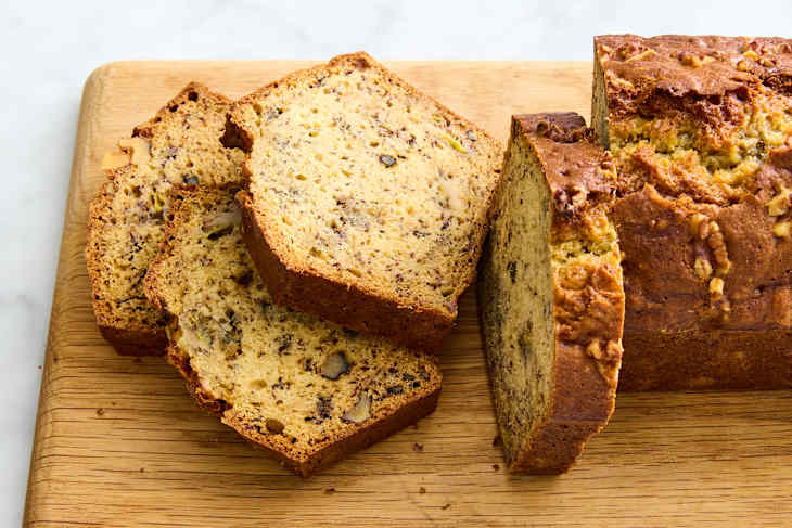 banana bread on brown parchment on wire rack with slices falling off
