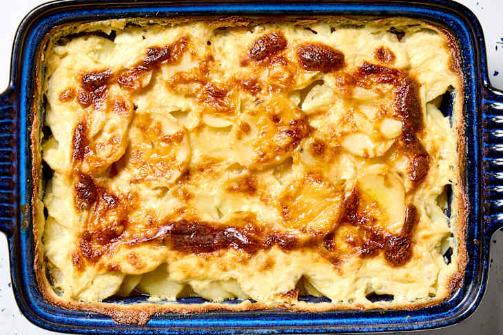 overhead shot of scalloped potatoes in a dark blue baking dish.