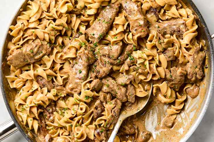 overhead shot of beef stroganoff and egg noodles in a stainless steel pan.