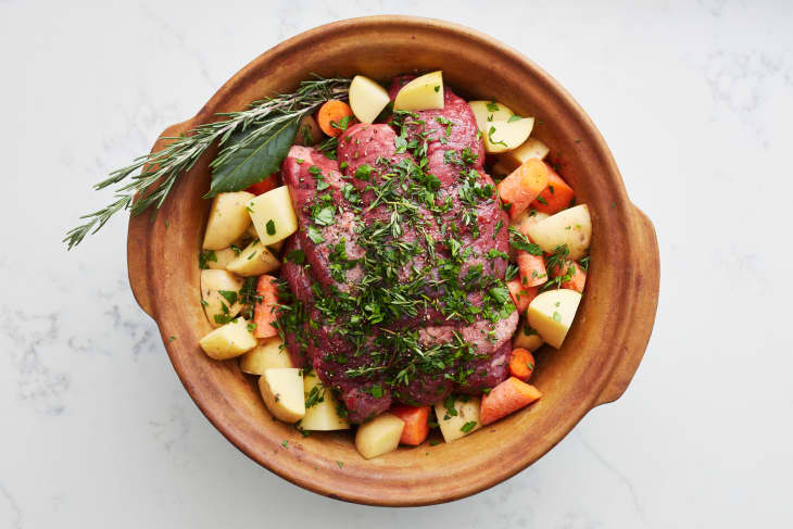 beef sits on top of vegetables and herbs in a clay pot