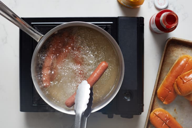 Hot dog being pulled from pot of boiling water.