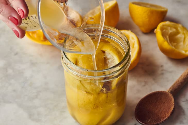 someone adding lemon juice to a mason jar filled with lemons