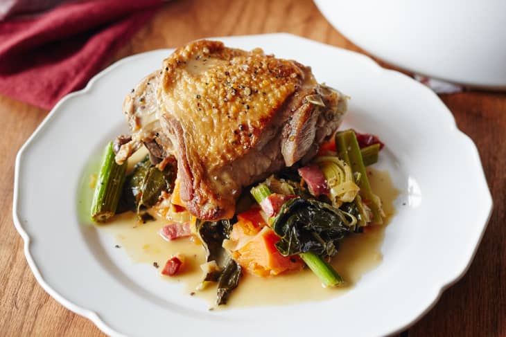 Braised turkey thigh on a white plate with leeks, greens, and bacon.