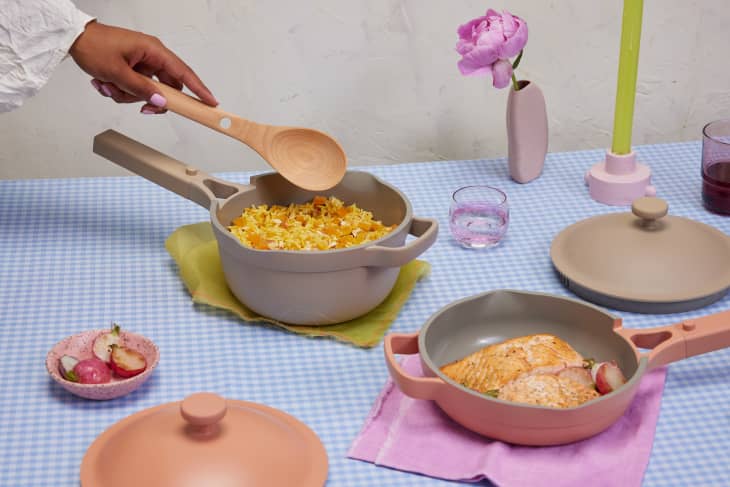 Cookware with rice and salmon on a checkered tablecloth, surrounded by a pink vase, candle, and glass.