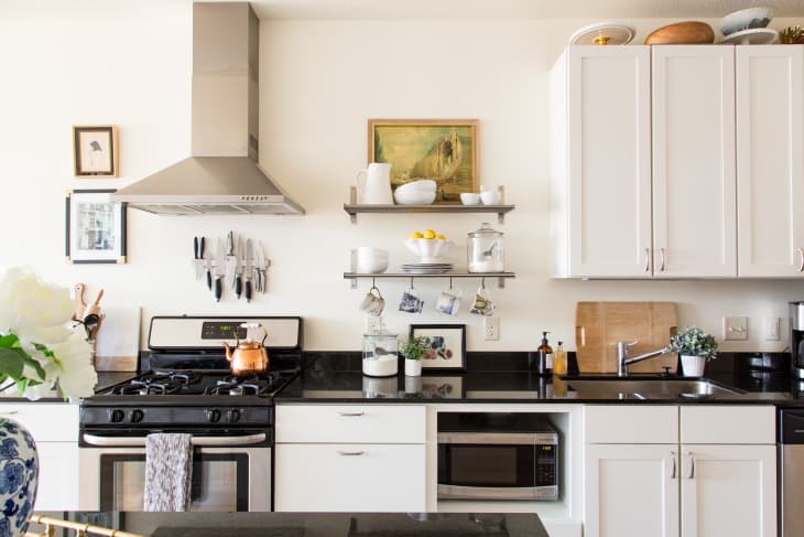 Modern kitchen with white cabinets, black countertops, stainless steel stove, and decorative shelves with plants and dishes.