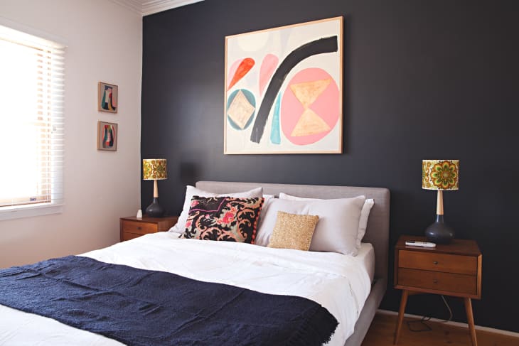 Bedroom with dark accent wall, abstract art, two wooden nightstands, patterned lamps, and a bed with decorative pillows.
