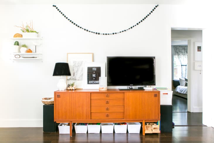 Mid-century modern console with TV, black lamp, framed art, and decorative items, flanked by shelves and doorway to bedroom.