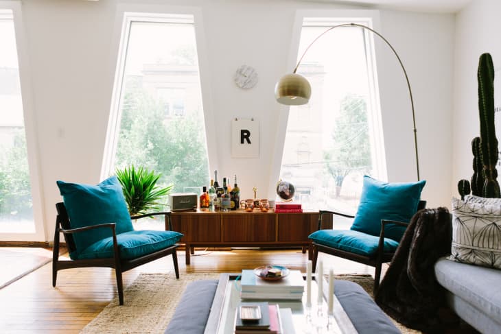 Mid-century modern living room with blue cushioned chairs, wooden sideboard, and large windows.