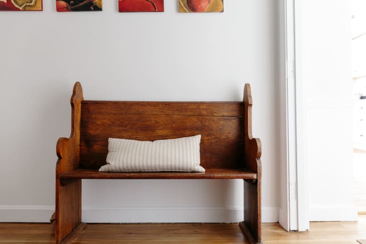 Wooden bench with a striped cushion against a white wall, beneath colorful abstract paintings.
