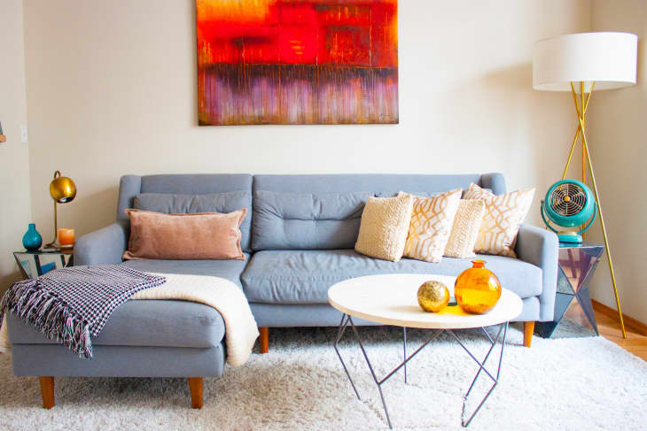 Gray sofa with assorted pillows, abstract red artwork, round white table, and modern floor lamp in a cozy living room.