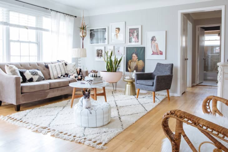 Bright living room with beige sofa, gray armchair, white rug, wall art, and a small dog on a pouf.