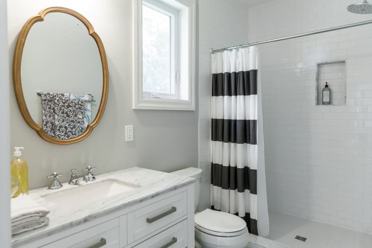 Bathroom with marble countertop, oval mirror, striped shower curtain, and white subway tiles.