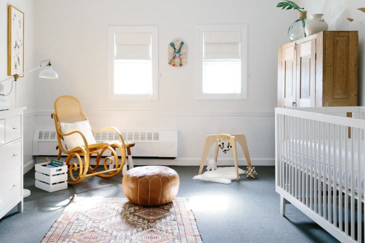 Nursery with a wooden rocking chair, white crib, leather pouf, and play gym on a patterned rug.