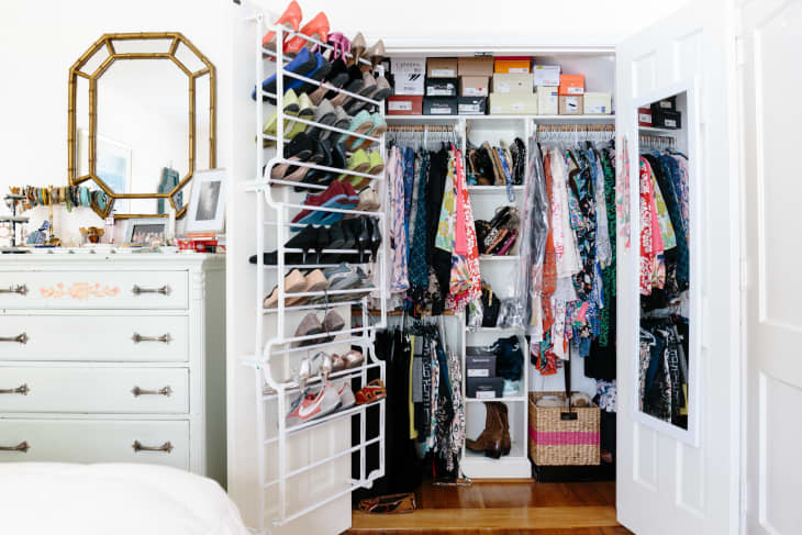 Open closet with colorful clothes, shoes on racks, and boxes on shelves, next to a white dresser with a mirror.