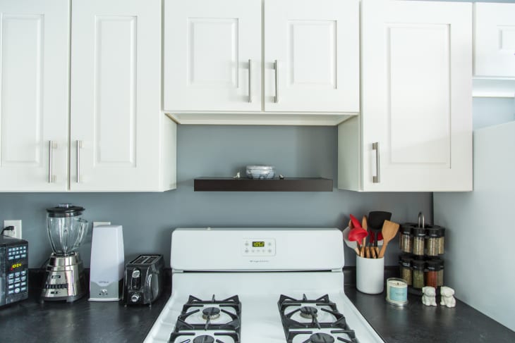 White kitchen cabinets above a stove with utensils, spices, blender, and microwave on the countertop.