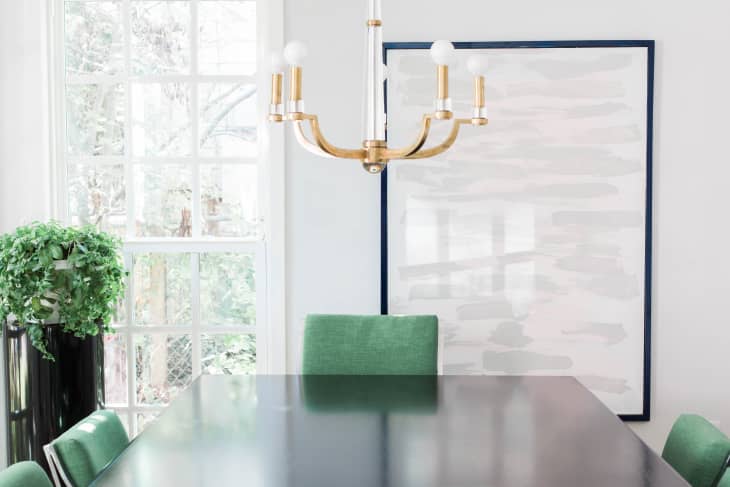 Dining room with green chairs, black table, gold chandelier, large window, and abstract wall art.