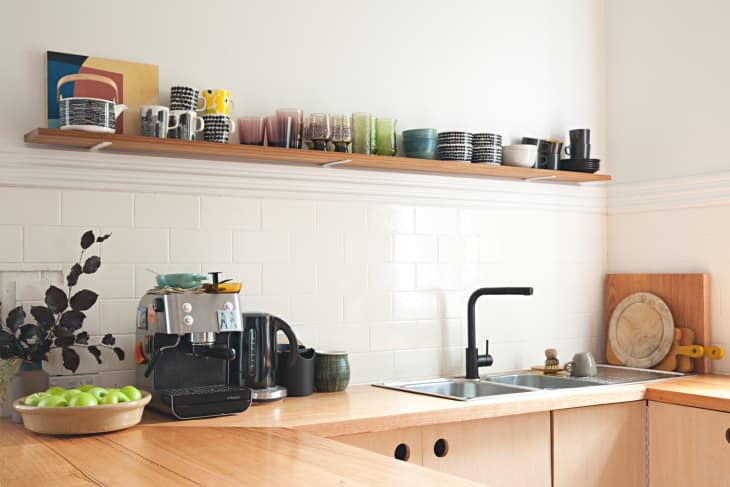 Cups and bowls sitting on a floating shelf above a sink in a retro kitchen