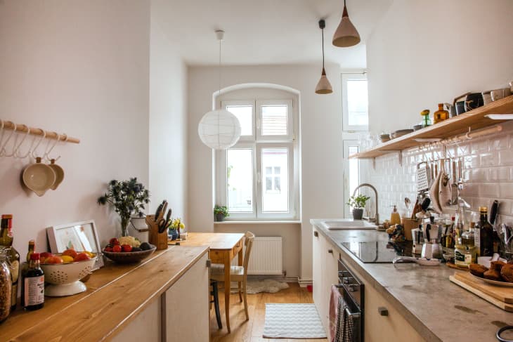 Narrow kitchen with wooden countertops, hanging pendant lights, and a small dining table by a window.