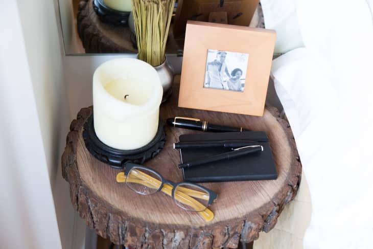 Wooden side table with a candle, glasses, pens, and a framed black-and-white photo.