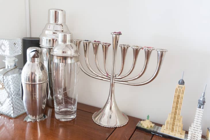 Silver menorah on a wooden table with cocktail shakers and New York City model buildings.