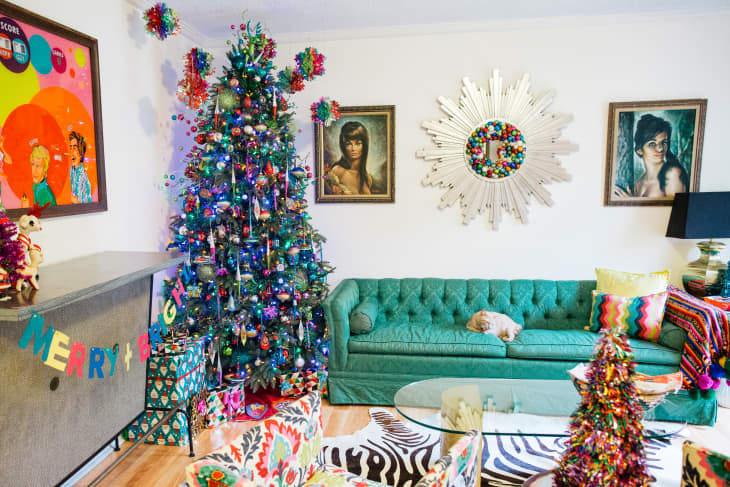 Colorful living room with a decorated Christmas tree, green sofa, vibrant artwork, and a sunburst mirror on the wall.