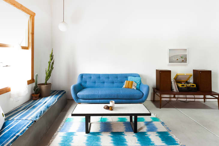 Living room with blue sofa, patterned rug, coffee table, cactus, and record player on a wooden console.