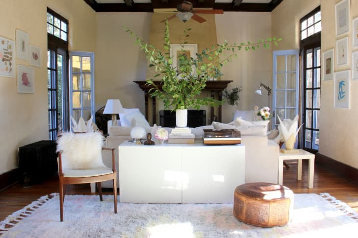 Living room with white sofa, large plant centerpiece, wooden chair, and decorative art on walls.